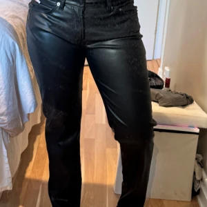Svarta skinnbyxor från 157, stl M - Snygga svarta byxor i skinnimitation från 157. Klassisk femficksmodell med raka ben och normal passform. Byxorna har bälteshällor och dragkedja med knapp framtill. Perfekta för dig som vill ha en edgy look.
