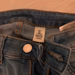 Bootcut jeans från &Denim, ljusblå - Ljusblå bootcut jeans från &Denim med låg midja. Klassisk femficksmodell med dragkedja och knapp framtill. Jeansen har snygga slitningar och kontrastsömmar, perfekta för en avslappnad look. Skickar såklart bilder ifall det skulle önskas. 