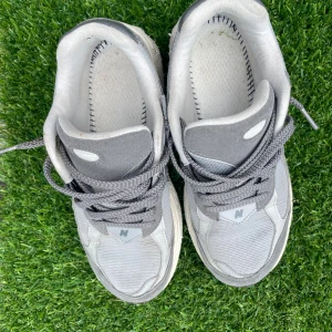 Grå New Balance 2002R sneakers - Snygga New Balance 2002R sneakers i olika grå nyanser med mesh och mocka-paneler. Skorna har den klassiska N-loggan på sidorna, snörning och en chunky sula med svart och vit detalj. Perfekta för dig som gillar retrovibbar och streetstyle.