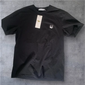 Svart t-shirt från Maison Kitsuné - Snygg svart t-shirt från Maison Kitsuné. Helt ny från NK Göteborg. Nypris 1000kr. Gjord med en liten broderad logga på bröstet. Perfekt för en stilren look. Kortärmad och tillverkad i mjukt material för extra komfort.
