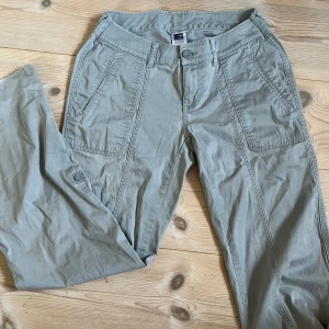 Ljusgröna cargopants från The North Face - Säljer ett par ljusgröna cargopants från The North Face med raka ben och stora fickor framtill. Byxorna har låg midja och är tillverkade i bomull, perfekta för en chill och avslappnad stil. Snygga detaljer med knappar vid benslut och klassisk logga på knappen.