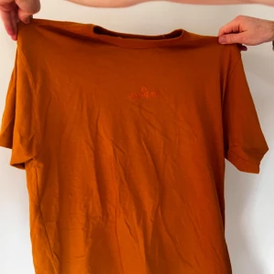 Orange t-shirt från Stone Island - Snygg orange t-shirt från Stone Island med diskret broderad logga på bröstet. Modellen är klassisk med rund hals och korta ärmar. Perfekt för dig som gillar cleana och stilrena plagg med lite edge. Materialet är mjuk bomull som känns skönt mot huden.