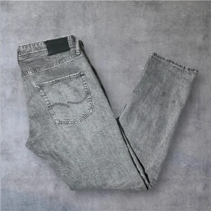 Grå jeans från Jack & Jones - Snygga grå jeans från Jack & Jones med klassisk femficksdesign och svarta detaljer på bakfickorna. Jeansen har en rak passform och är tillverkade i slitstarkt denim. Perfekta för dig som gillar en avslappnad men stilren look. Riktigt snygg grå fade, Inga tecken på användning, modellen är tapered mike, slim fit (sitter som ett par replay anbass, nudie grim Tim eller nudie Lean Dean. Storlek 31/32 passar 175-185. 