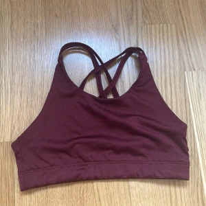 Vinröd sportig linnetopp med korsade band - Säljer en vinröd linnetopp med smala korsade axelband i ryggen. Toppen är enkel och stilren, perfekt för träning eller chill. Materialet är mjukt och stretchigt för bästa komfort. Snygg detalj med liten logga bak. Storlek 146-152