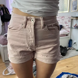 Ljusrosa jeansshorts från 157 - Säljer ett par ljusrosa jeansshorts från 157 med klassisk femficksmodell, hög midja och knappgylf. Shortsen har råa kanter nertill och är tillverkade jeanstyg. Perfekta för varma dagar och enkel att matcha med allt.