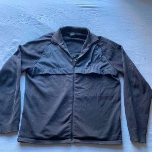 Svart ziptröja från BOSS - Snygg svart ziptröja från BOSS med hög krage och diskret logga framtill samt stor BOSS-text på ryggen. Tröjan har hel dragkedja, långärmade ärmar och är gjord i en blandning av bomull och polyester. Perfekt för lager-på-lager och chill vardagsstil.