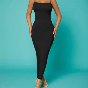 Svart långklänning med smala axelband - Supersnygg svart långklänning med smala axelband och figurnära passform. Klänningen har en rak halsringning och korsade band i ryggen som ger en cool detalj. Perfekt för dig som gillar minimalistisk stil och vill ha en enkel men elegant look.