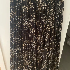 Svart långkjol med beige mönster - Säljer en svart långkjol med beige prickigt mönster och plisserad design. Kjolen har en flowy känsla och passar perfekt till sneakers eller boots. Resår i midjan för skön passform. Superenkel att styla till olika looks.