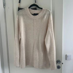 Beige stickad tröja från Gina Tricot - Supermjuk beige stickad tröja från Gina Tricot i oversized modell. Tröjan har bred ribbad mudd vid ärmslut och nederkant samt en snygg söm mitt fram. Perfekt för lager-på-lager och chill dagar.
