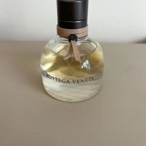 Bottega Veneta Eau de Parfum 30 ml Använd - Använd Elegant parfym från Bottega Veneta i en rund glasflaska med ljusbeige band och svart kork. Flaskan har ett diskret rutmönster i glaset och parfymen är ljusgul. Perfekt för dig som gillar lyxiga och sofistikerade dofter.