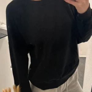Svart sweatshirt från Cubus - En klassisk svart sweatshirt från Cubus i ekologisk bomull. Tröjan har rund halsringning och långa ärmar, perfekt för en enkel och stilren look. Passar dig som gillar basic och bekväma plagg.