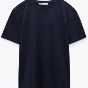 Mörkblå t-shirt från Zara - En stilren mörkblå t-shirt från Zara med klassisk rund halsringning och korta ärmar. Perfekt enkel baströja i mjuk bomull som passar till det mesta. Snygg att matcha med jeans eller shorts.