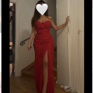Röd långklänning med slits och hjärtformad urringning - Säljer en elegant röd långklänning med hjärtformad urringning och  slits framtill. Klänningen är axelbandslös och har en figurnära passform som framhäver siluetten. Perfekt för bal eller festkvällar. Fallet på klänningen är magisk.Storlek S.