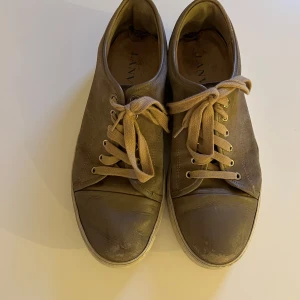 Bruna sneakers från Lanvin storlek 10/43 - Säljer ett par bruna sneakers från Lanvin med beige snörning och vit sula. Ordentligt använda men går att fräscha upp genom att tvätta. Box finns även samt ett par nya skosnören.
