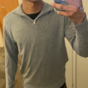 Grå halvzip-tröja från 1974 - Säljer en stilren grå långärmad tröja från 1974 med halv dragkedja vid halsen. Perfekt för lager-på-lager och enkel att matcha med olika outfits. Mjuk och bekväm, passar både till jeans och chinos.