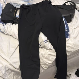 Svarta byxor från Mamalicious - Svarta byxor från Mamalicious i mjukt och stretchigt material. De har en enkel och stilren design med resår i midjan för extra komfort. Perfekta för en avslappnad och bekväm look.