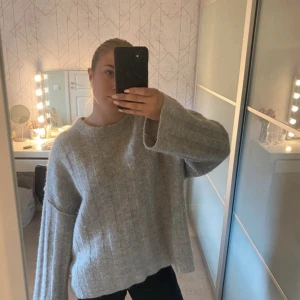 Grå stickad tröja från Gina Tricot - Mysig grå stickad tröja från Gina Tricot med breda ärmar och rund halsringning. Tröjan har en lätt oversized passform och ribbad struktur som ger en stilren look. Perfekt för lager-på-lager under kyliga dagar.