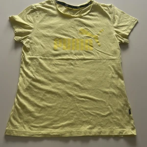 Gul t-shirt från Puma - Säljer en ljusgul t-shirt från Puma med klassisk logga tryckt framtill i gult. T-shirten har rund halsringning och korta ärmar. Perfekt för en sportig och avslappnad stil. Aldrig använt💛