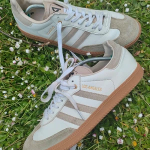 Adidas Los Angeles sneakers i vitt och beige - Säljer ett sällsynt par Adidas Los Angeles sneakers i vitt och beige med klassiska tre ränder på sidan och gummisula. Skorna har snörning och detaljer i mocka framtill och på sidorna. Perfekta för en stilren vardagslook. Ny pris kan ligga på ungefär 4000 då de är så sällsynta men säljer för lågt pris då jag använt de en del. Bara att höra av sig vid funderingar. De är äkta och jag kan komma med bevis ifall om det krävs