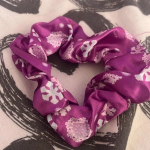 Lila frost scrunchie - En lila scrunchie i satinliknande material med vita snöflingor som mönster. Perfekt för att sätta upp håret med en färgglad och vintrig touch.