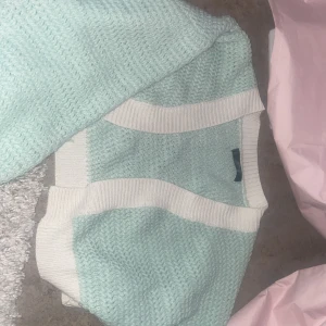 Stickad mintgrön väst med vita kanter - Superfin stickad väst i mintgrönt med breda vita ribbade kanter. Perfekt att styla över en klänning på sommaren eller t-shirt för en trendig lager-på-lager-look. Koftan är mjuk och bekväm och passar perfekt till sommaren. Den är i bra skick och typ aldrig använt den, har bara för mycket kläder därför jag säljer den. 