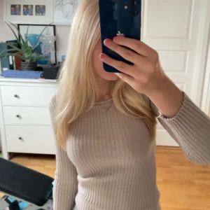 Beige ribbad långärmad topp - Säljer en beige ribbad långärmad topp med rund halsringning. Tröjan är figurnära och har ett stilrent, enkelt utseende som passar perfekt till jeans eller kjol. Materialet är mjukt och stretchigt för en bekväm passform. Tröjan är även lite glittrig så passar även till finare tillfällen! Tror tröjan är från hm men fick den av en vän! Säljer pgr av att den är för kort vid armarna🥰🎀