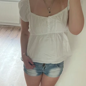 Vit blus med puffärmar och knappar - Söt vit blus med korta puffärmar och knappar framtill. Blusen har en lös passform och en lätt rynkad detalj under bysten. Perfekt för varma dagar och enkel att matcha med jeansshorts.