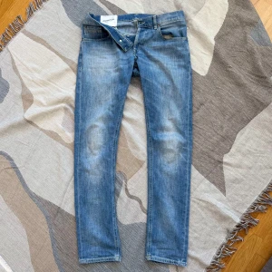 Blå jeans från Dondup - Säljer ett par klassiska blå jeans från Dondup med normal passform och raka ben. Jeansen har fem fickor, knappgylf och snygga slitningar framtill. Perfekta till vardags och enkla att matcha med olika stilar. Jeansen är i storlek 32!