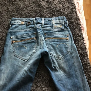 Blå jeansbyxor från G-Star  - Säljer ett par blå jeansbyxor från G-Star med snygga dragkedjor på bakfickorna och dekorativa sömmar. Klassisk femficksmodell med normal passform och låg midja. Dom är raka. Mer som slim. Säljer då domningar passar mig. Använt en gång. PRISET KAN DISKUTERAS!!!💗💗
