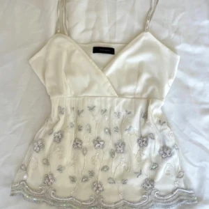 Stockholmstyle vintage top - Säljer en romantisk vit linnetopp med smala axelband och v-ringning. Toppen har vackra broderade blommor, pärlor och paljetter nertill samt transparent mesh med vågig kant. Perfekt för sommarens alla tillfällen! Jag betalade 35€ för detta. Jag köpte från vinted men den var stor för mej. 