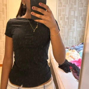 Svart topp - Säljer en svart topp med korta ärmar och rund halsringning. Toppen har en snygg öppen rygg med knytband som detalj. Aldrig använd, jättebra i stick