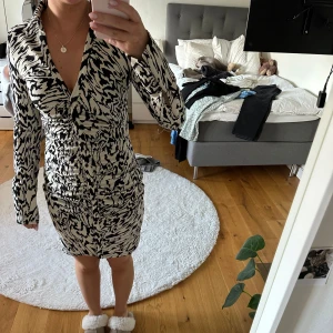 Svartvit mönstrad skjortklänning - Säljer en svartvit skjortklänning med djurmönster och v-ringning. Klänningen har lång ärm, krage och snygg rynkdetalj framtill. Klänningen är aldrig använd och har precis tagit av prislappen. Den är från hm och är i storlek S 