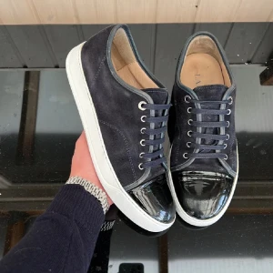 Navy blue lanvins dbb1  - Säljer ett par mörkblåa sneakers med vit sula och snygg lackad tå. Ovandelen är i mocka och skorna har klassisk snörning. Perfekta för dig som vill ha en stilren men ändå unik look. Box och tillbehör medföljer