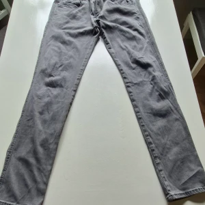 Grå jeansbyxor från Replay Anbass - Säljer ett par grå jeansbyxor från Replay, modell Anbass. Byxorna har klassisk femficksdesign, raka ben och normal passform. Snygga detaljer med Replay-logga på bakfickan och läderpatch i midjan. Perfekta till vardags för en stilren look.