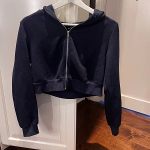 Mörkblåcroppad hoodie med dragkedja - En mörkblå croppad hoodie med dragkedja framtill och långa ärmar. Perfekt för en avslappnad stil och enkel att matcha med jeans eller leggings. Mjuk och bekväm med huva.