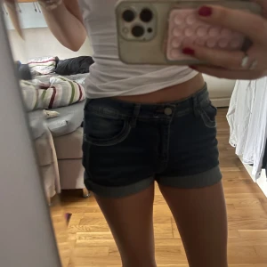 Mörkblå lågmidjadd  jeansshorts - Säljer ett par mörkblå jeansshorts med klassisk femficksdesign och uppvikta benslut. Shortsen har låg midja och detaljerade bakfickor. Aldrig använda❣️Supersnygga fickor