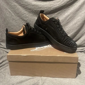 Svarta sneakers med nitar från Christian Louboutin - Säljer ett par svarta sneakers från Christian Louboutin med mattsvarta nitar på tån och klassisk röd sula. Skorna har snörning och är tillverkade i skinn med en lyxig känsla. Perfekta för dig som vill sticka ut med en exklusiv look. HELT NYA Kan snacka om pris 