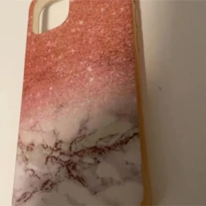 Rosa och vit marmormönstrad sjal iPhone 12 mini - Säljer ett snyggt mobilskal med rosa glittereffekt upptill och vit marmordesign nedtill. Skalets material känns som syntet och det har en modern look som passar till de flesta mobiler. Perfekt accessoar för dig som vill ha något unikt och trendigt. För iPhone 12 mini 