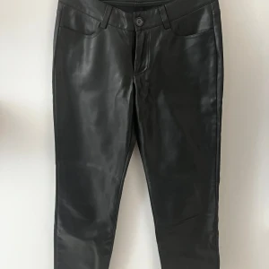 Svarta skinnbyxor - Snygga svarta byxor i skinnimitation (straight legs) fit och klassisk femficksdesign. Byxorna har normal midja, bälteshällor och stängs med knapp och dragkedja. Perfekta för en edgy och trendig look.