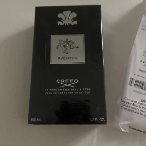 Creed Aventus Eau de Parfum 100ml - Exklusiv Creed Aventus Eau de Parfum i 100ml flaska. Snygg svart kartong med silverdetaljer och ikonisk logga. Parfymen är känd för sin fräscha, fruktiga och maskulina doft. Perfekt för dig som vill sticka ut med en lyxig och tidlös signaturdoft.