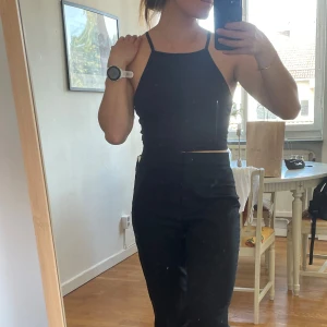 Svart croppad topp - Säljer en svart croppad topp från Divided med smala axelband och rak halsringning. Toppen är tight och sitter snyggt mot kroppen, perfekt till höga byxor eller kjol. Enkel och stilren design som funkar till många olika looks.