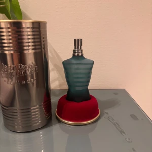 Jean Paul Gaultier Le Male parfym - Ikonisk parfymflaska i form av en blågrön manlig torso med frostad glasfinish och horisontella ränder. Kommer med original metallburk i silverfärg och röd sammetsbas. En klassiker med unik design som sticker ut i badrumshyllan.