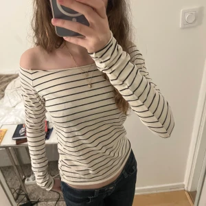 Randig offshoulder topp - Säljer en stilren randig offshoulder topp i beige och svart. Toppen har långa ärmar och en tight passform, perfekt för en trendig look. Passar bra till både jeans och kjol. använd en gång bara! Priset går att diskuteras 🩷