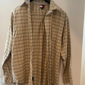 Beige rutig skjorta Tommy Hilfiger - Snygg beige rutig skjorta från Tommy Hilfiger i 100% bomull. Skjortan har klassisk krage, knäppning framtill och diskret logga på bröstfickan. Perfekt för dig som gillar en avslappnad men stilren look.