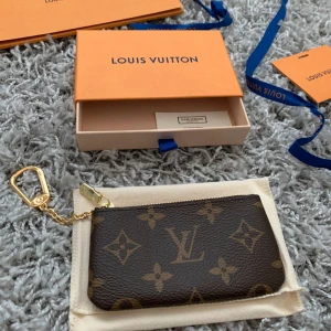 Louis Vuitton monogram key pouch - Säljer en oanvänd Louis Vuitton key pouch i brunt monogrammönster med guldiga detaljer och dragkedja. Kommer med original ask och dustbag. 