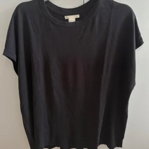 Svart oversized topp med liten slits på båda sidorna ä - En svart loose-fit topp från H&M. Modellen har korta ärmar och rund halsringning. Ribbad nederkant med liten slits på sidorna ger en chill vibe. Perfekt till jeans eller kjol för en enkel och stilren look