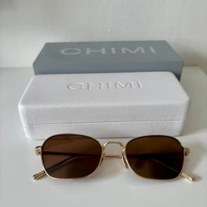 Chimi LYNX brun/guld solglasögon - Snygga solglasögon från Chimi i modellen LYNX med bruna linser och tunna guldfärgade metallbågar. Rektangulär form som ger en clean och modern vibe. Kommer med originaletui och box.                        Använda ett fåtal gånger, skicket är som nytt. 