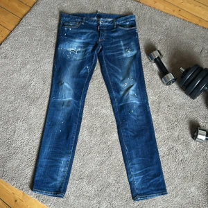 Blå distressed jeans från Dsquared2 - Säljer ett par blå jeans från Dsquared2 med coola slitningar, färgstänk och broderad D på bakfickan. 