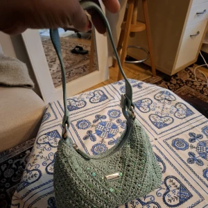 Mintgrön axelväska från Accessorize - Söt mintgrön axelväska i stickad look från Accessorize. Väskan har paljettdetaljer, silverfärgade metalldelar och dragkedja upptill. Perfekt storlek för det viktigaste och ger en chill vibe till din outfit.