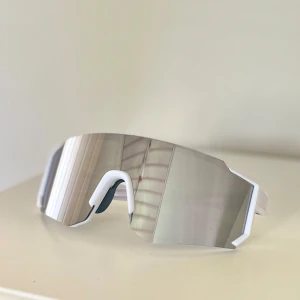 Snygga vita sportiga spegelglasögon - Säljer ett par futuristiska sportglasögon med vit båge och stora spegelblanka linser🤵🏼 De har en skarp, kantig design och sitter tight runt ansiktet – perfekta för dig som vill sticka ut på cykeln eller löprundan💪
